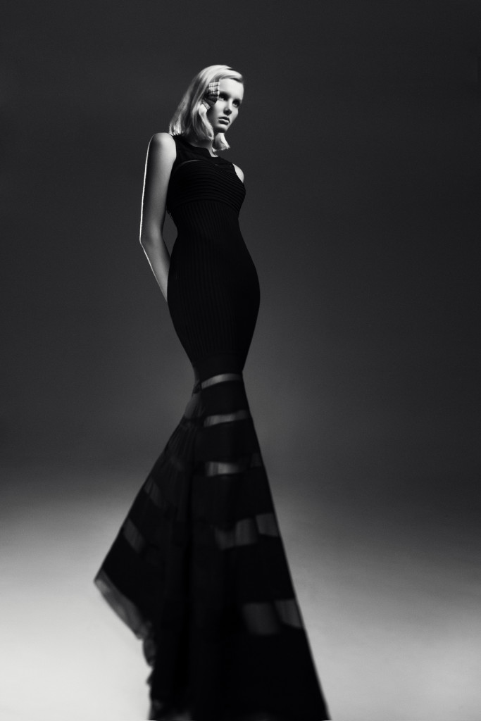 Model standing in a studio photographic shoot wearing a black dress with a fishtail.