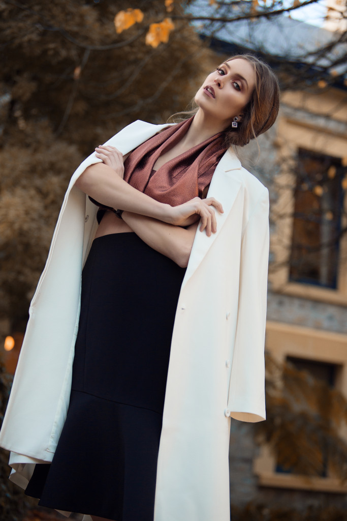 Model standing outside with arms crossed and a white jacket around her shoulders.j