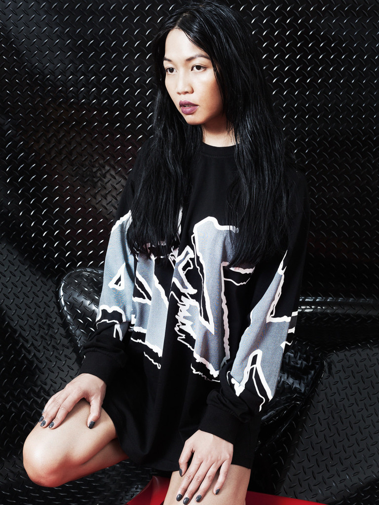Autumn/Winter 2015 Campaign. Asian girl sitting in an ASSK sweater with black and white textured wall behind.