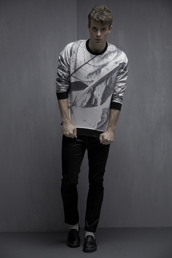 Male model standing in front of a grey wall in black pants and a digital print long sleeved T.