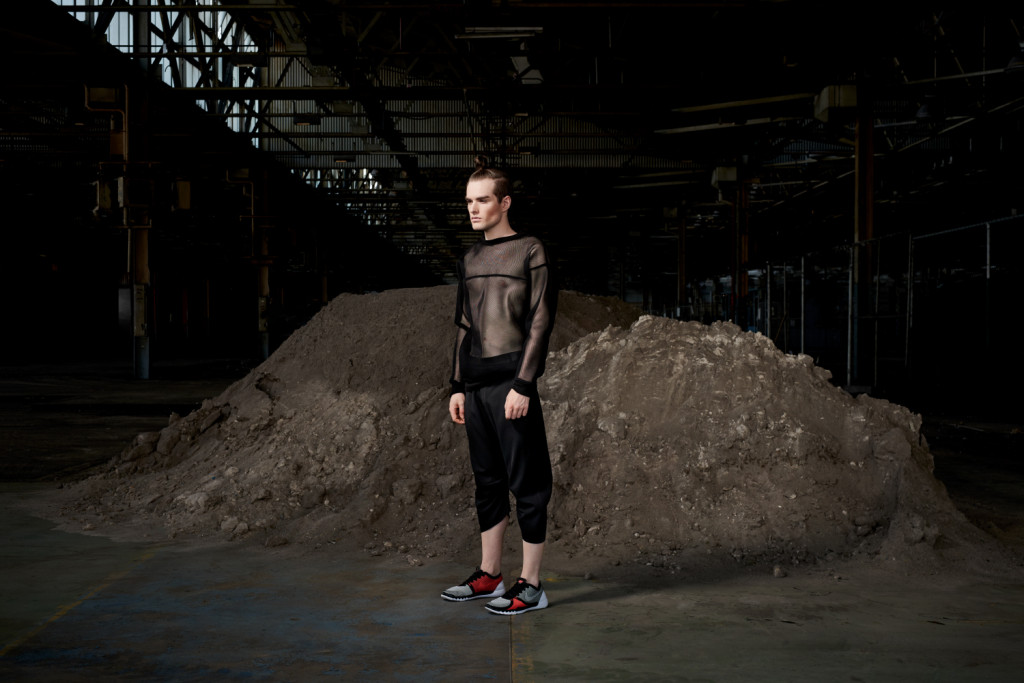 Model standing in an urban setting under a bridge dressed in the sports-luxe wear and technical fabric inspired by pop and internet culture, and elemental street styling.