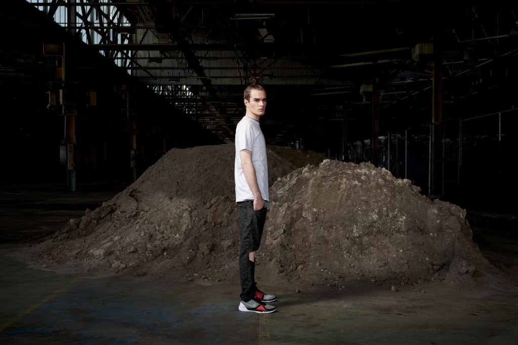 Model standing in an urban setting under a bridge dressed in the sports-luxe wear and technical fabric inspired by pop and internet culture, and elemental street styling.