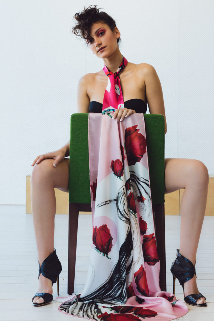 Model sitting for a photographic shoot for designer scarf label Valentina Avramides wearing a black strapless bra and covered in a scarf.