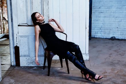 Girl sitting on a chair slouched back in a modelling shoot with black top, black leather pants and high black stilettos.